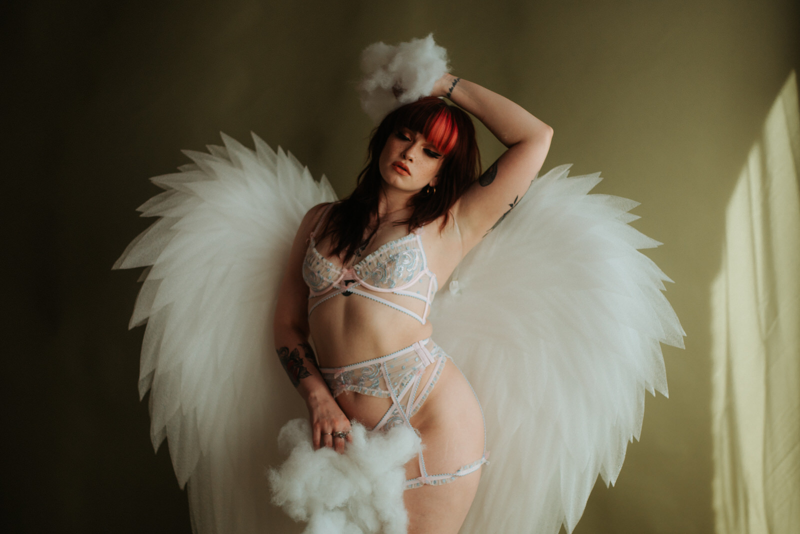 A woman in white lingerie wearing large angel wings for boudoir session in Dallas