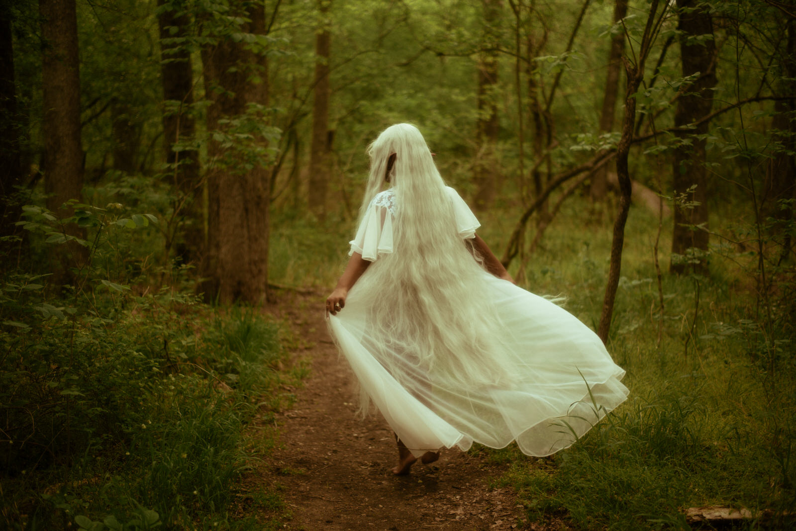 Elven woman with long white hair walking through the forest.
