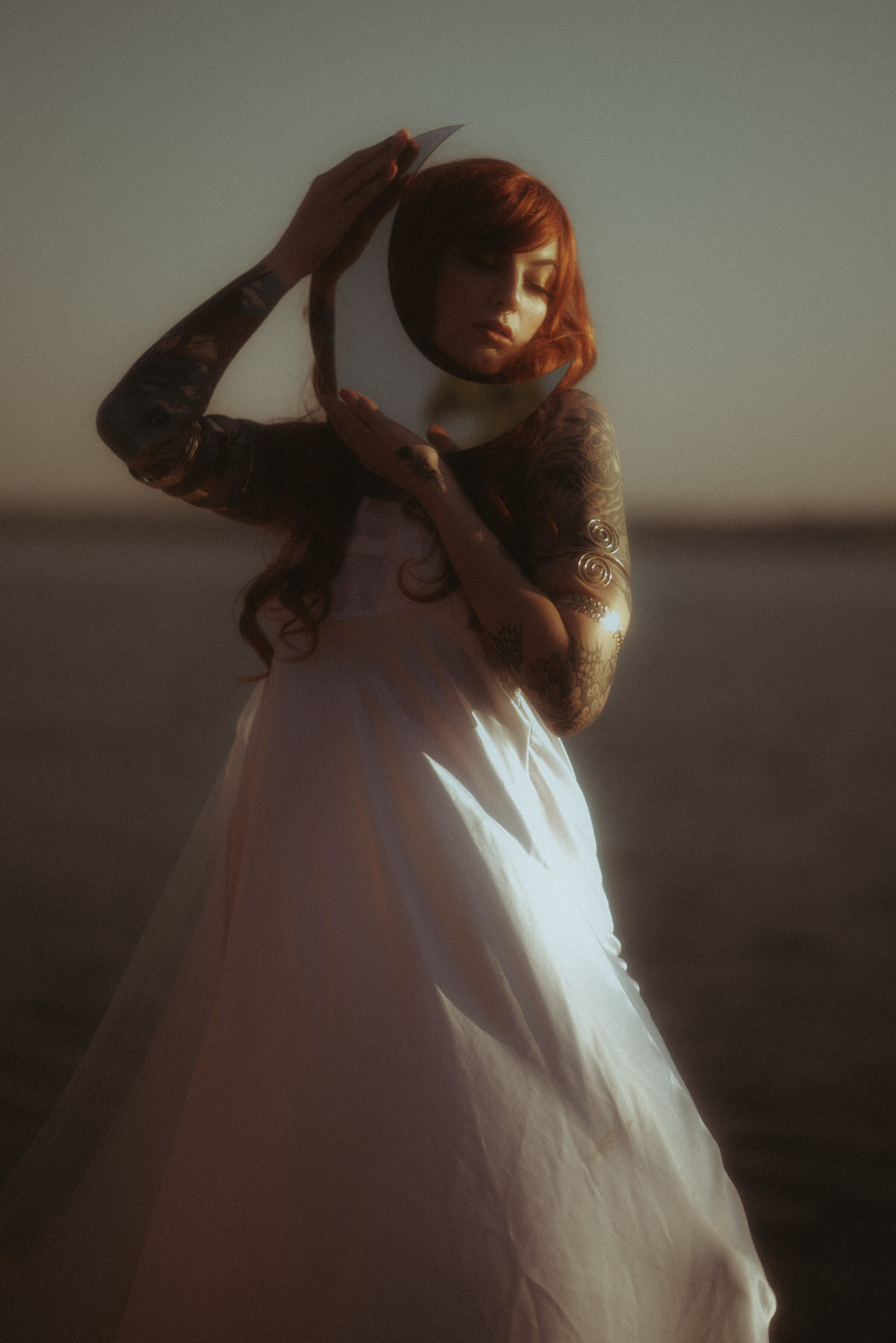 Model with red hair embracing the moon at the ocean.