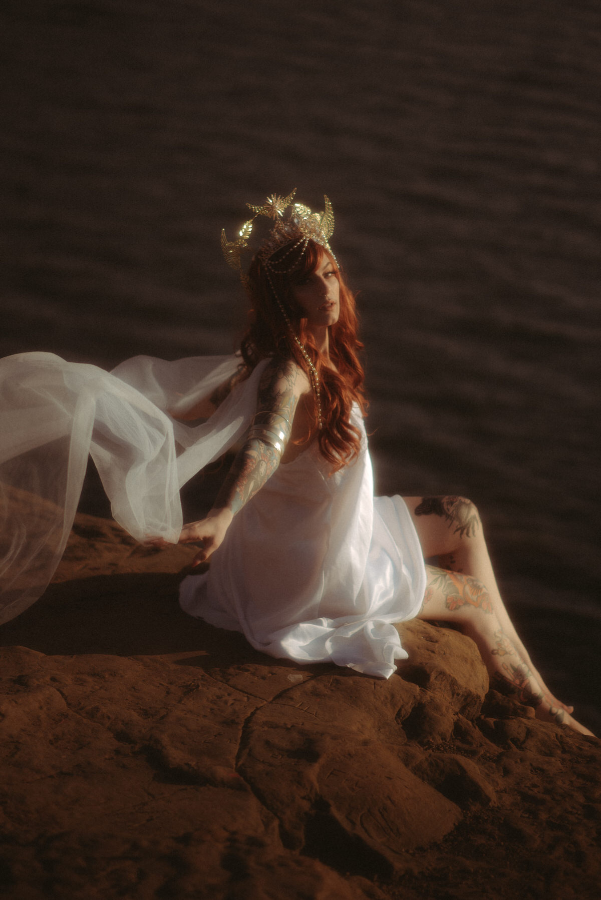Model sitting on a cliff at the ocean with fabric flying behind her.