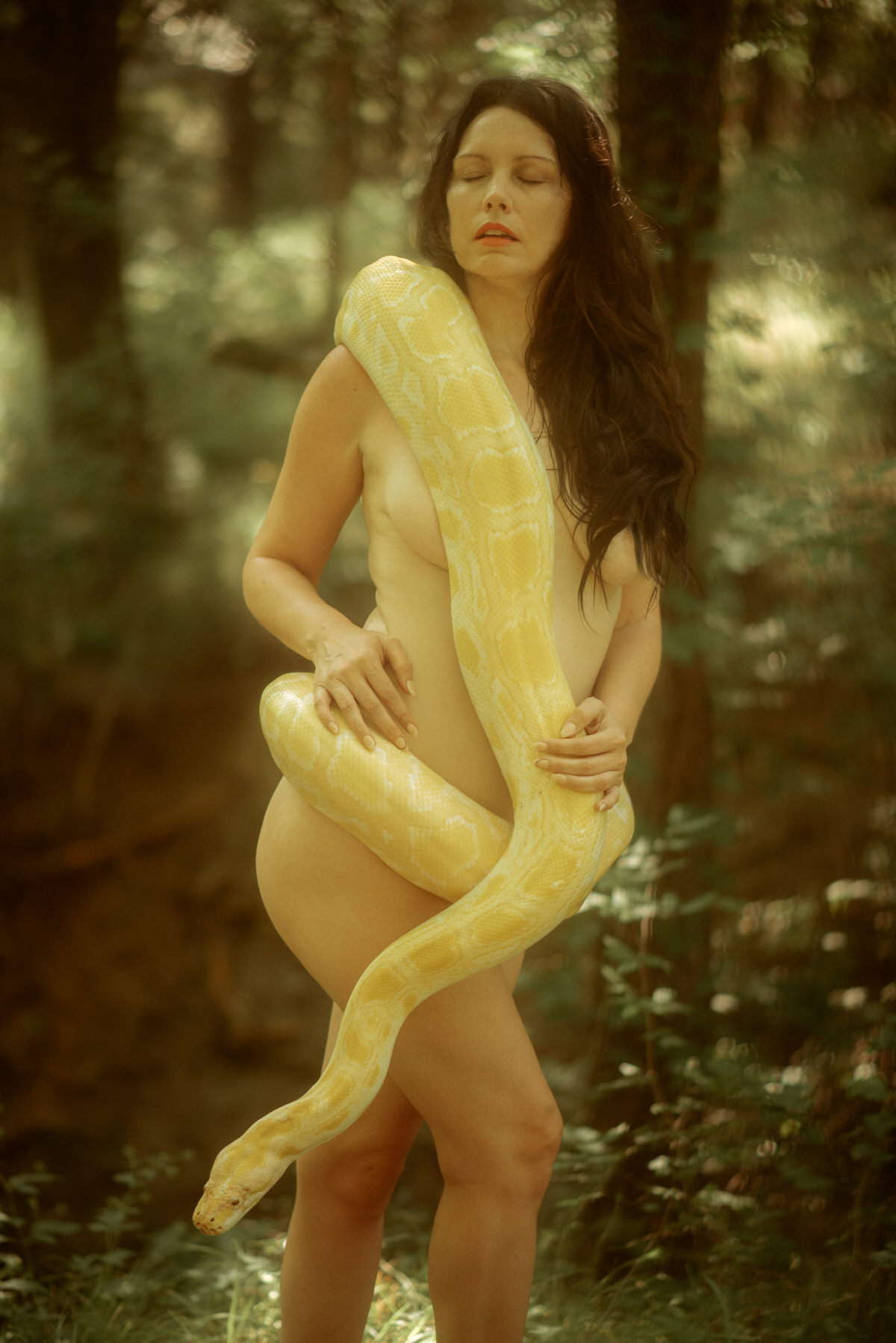 A woman in the forest holding a giant snake.
