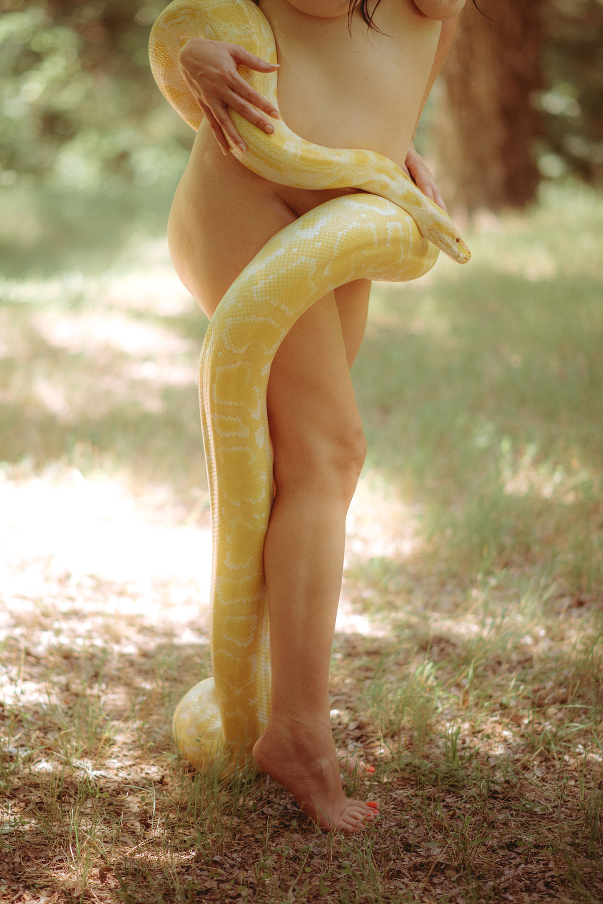 A nude woman holding a giant snake around her waist.