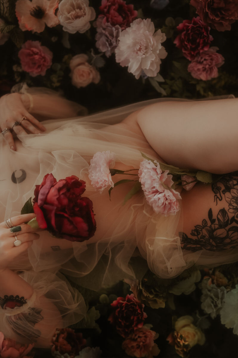 A woman lying down with moody flowers covering her body.