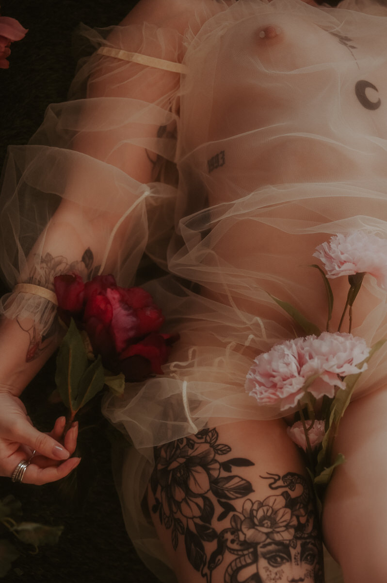 A nude woman laying down with flowers covering her naked body.