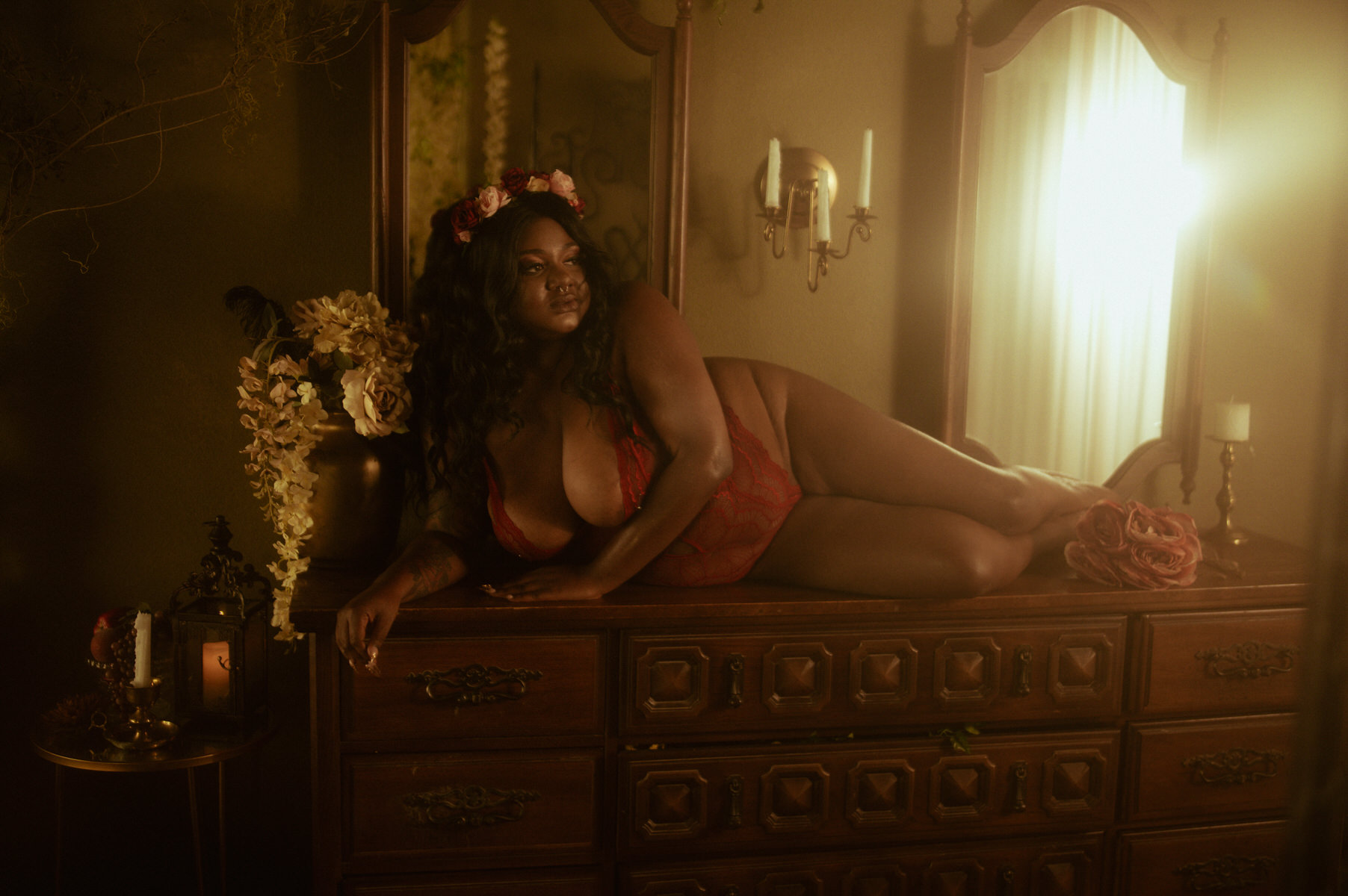 A woman in lingerie laying on a dresser in front of a mirror.