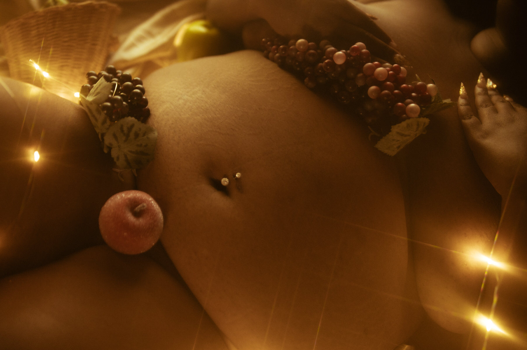 A woman laying on a bed with fruit on her stomach.