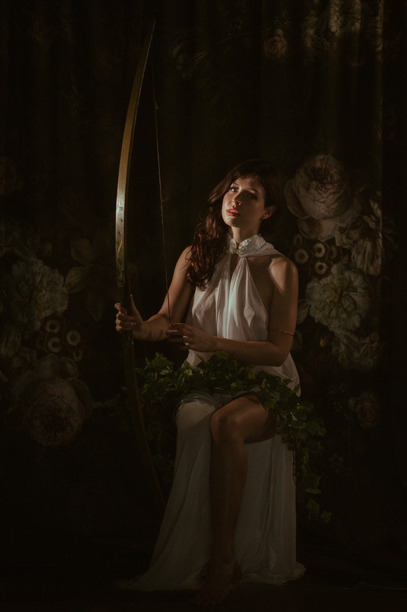 A woman in a white dress showcasing Dallas Boudoir Photography, while holding a bow and arrow.