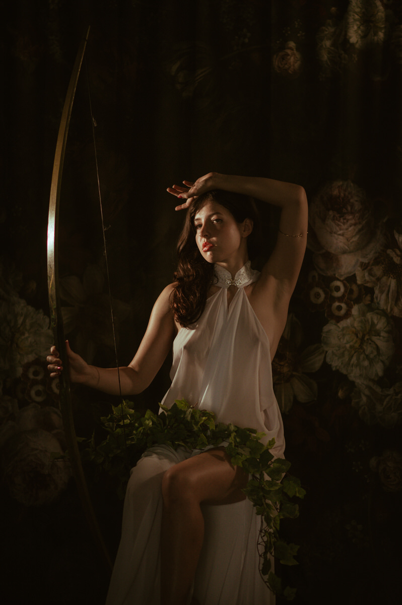 A woman in a white dress posing with a bow and arrow for Dallas Boudoir Photography.