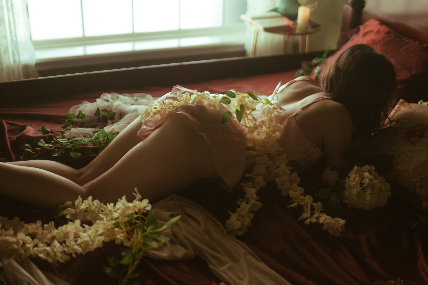 A Dallas woman posing on a bed adorned with flowers in a boudoir photoshoot.