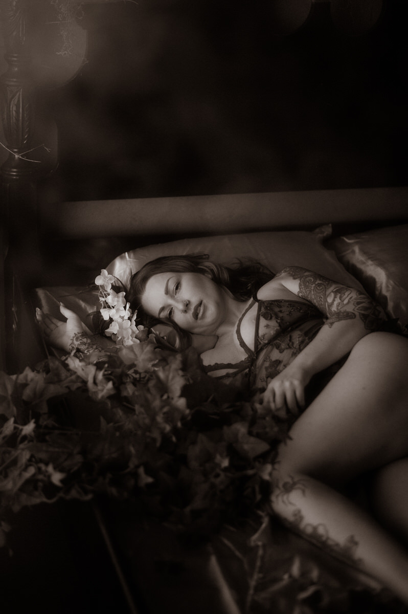 A woman is laying on a bed surrounded by flowers at a Dallas boudoir studio.