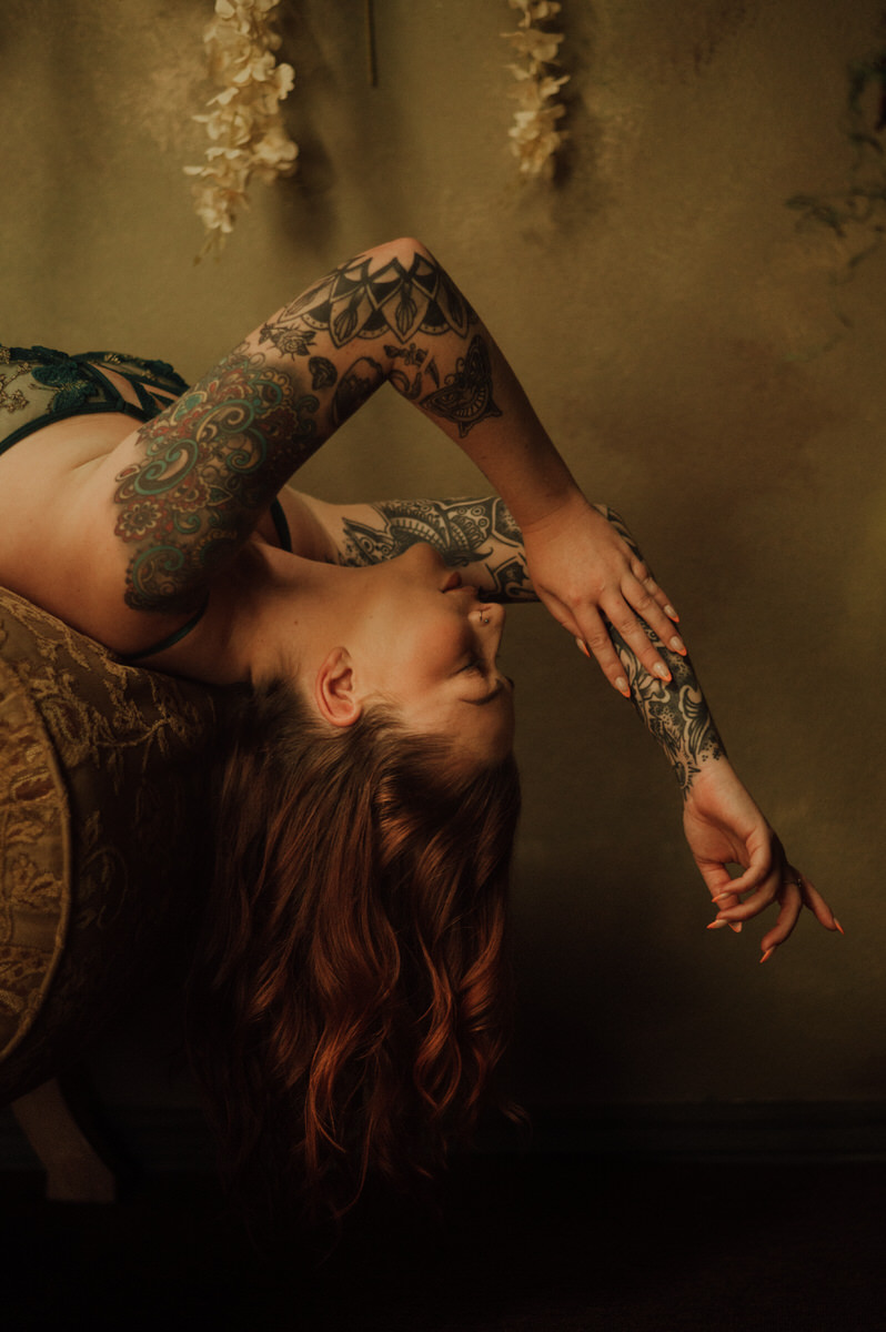 A woman with tattoos laying on a chair at a Dallas boudoir studio.