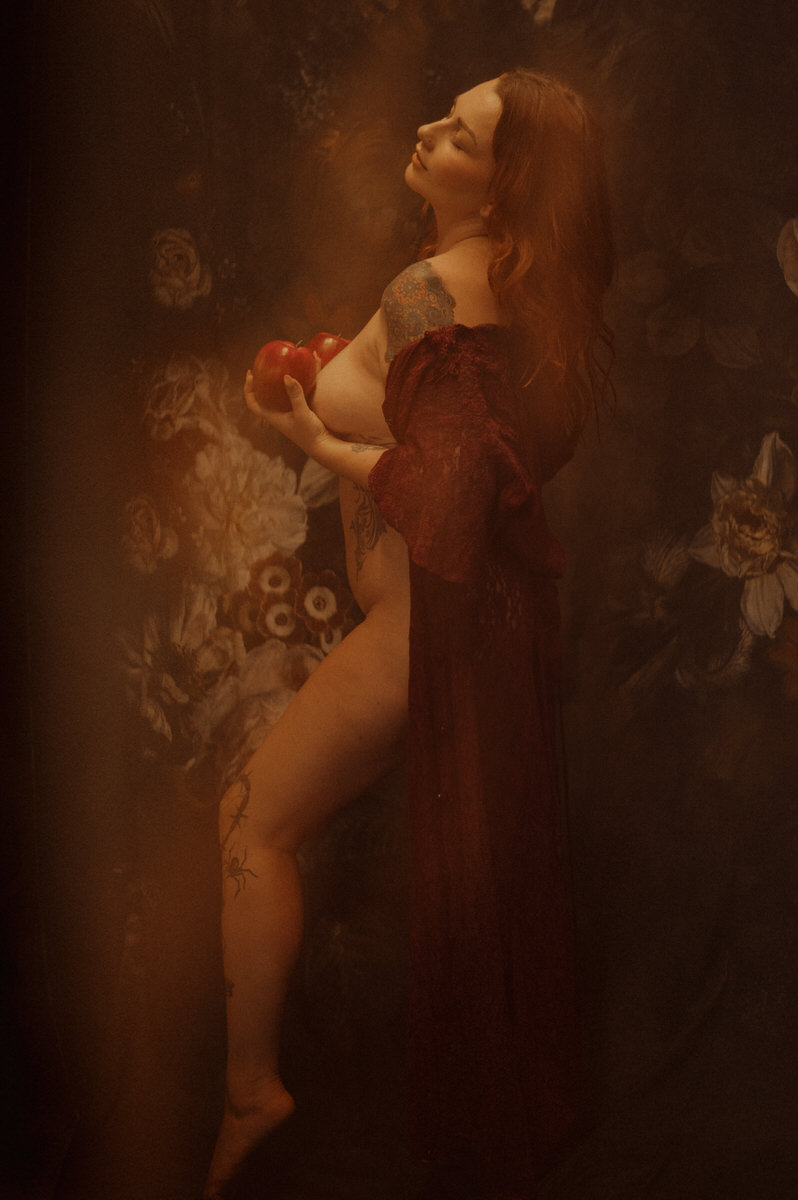 A Texas woman in a red dress posing sensually with an apple showcases the artistry of boudoir photography.