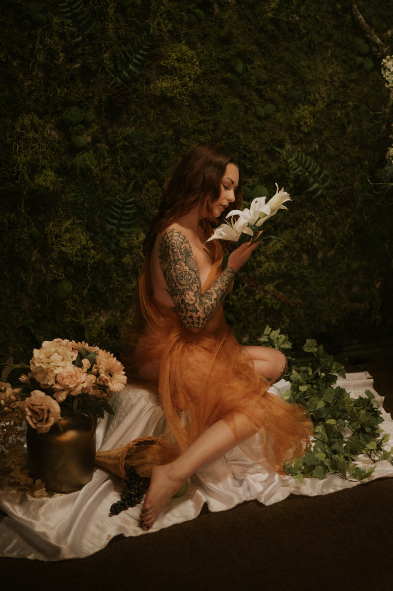 An artistic woman sitting on a bed, holding flowers in her hands at a Dallas boudoir studio.