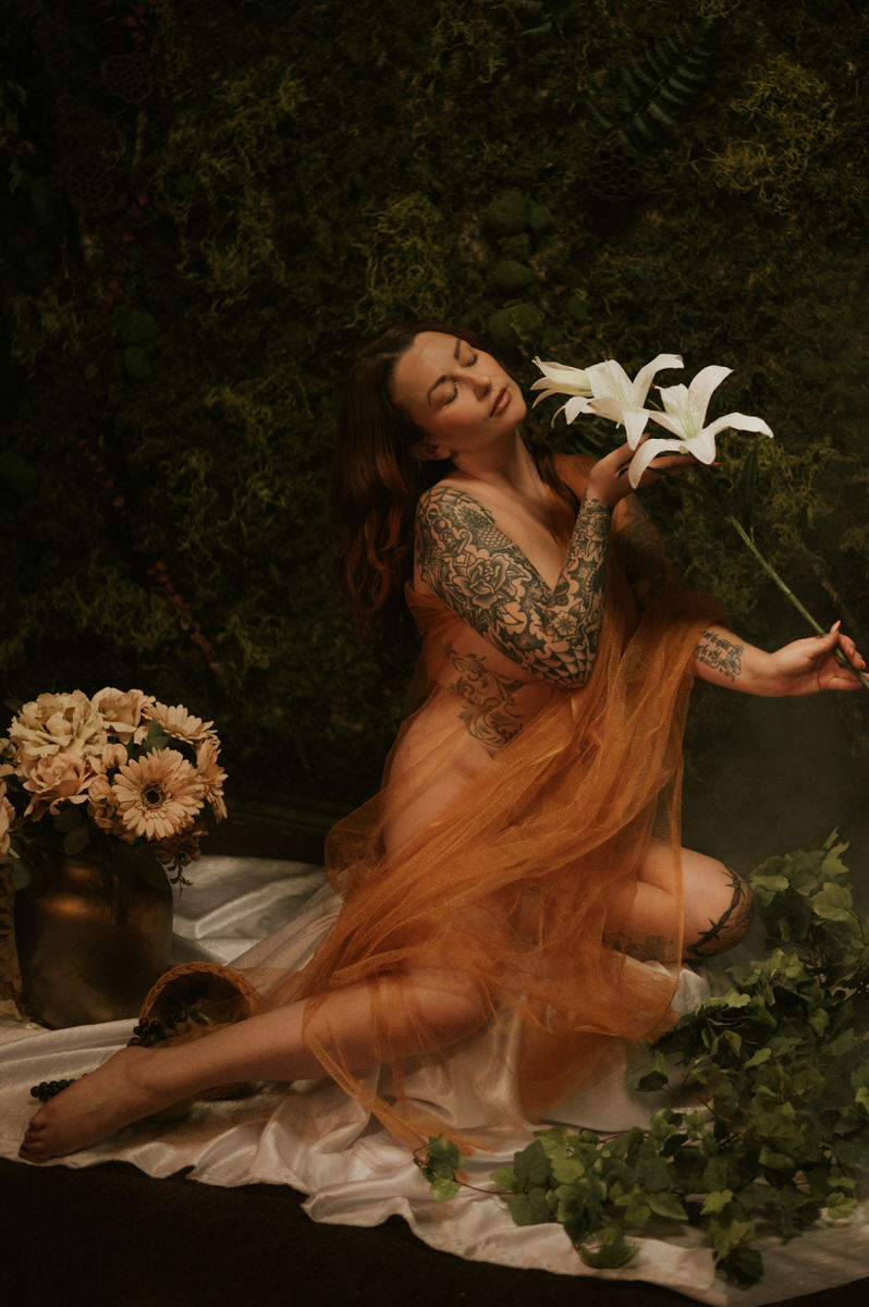 A woman in an orange tulle dress posing elegantly with a bouquet of flowers, capturing the essence of boudoir photography.
