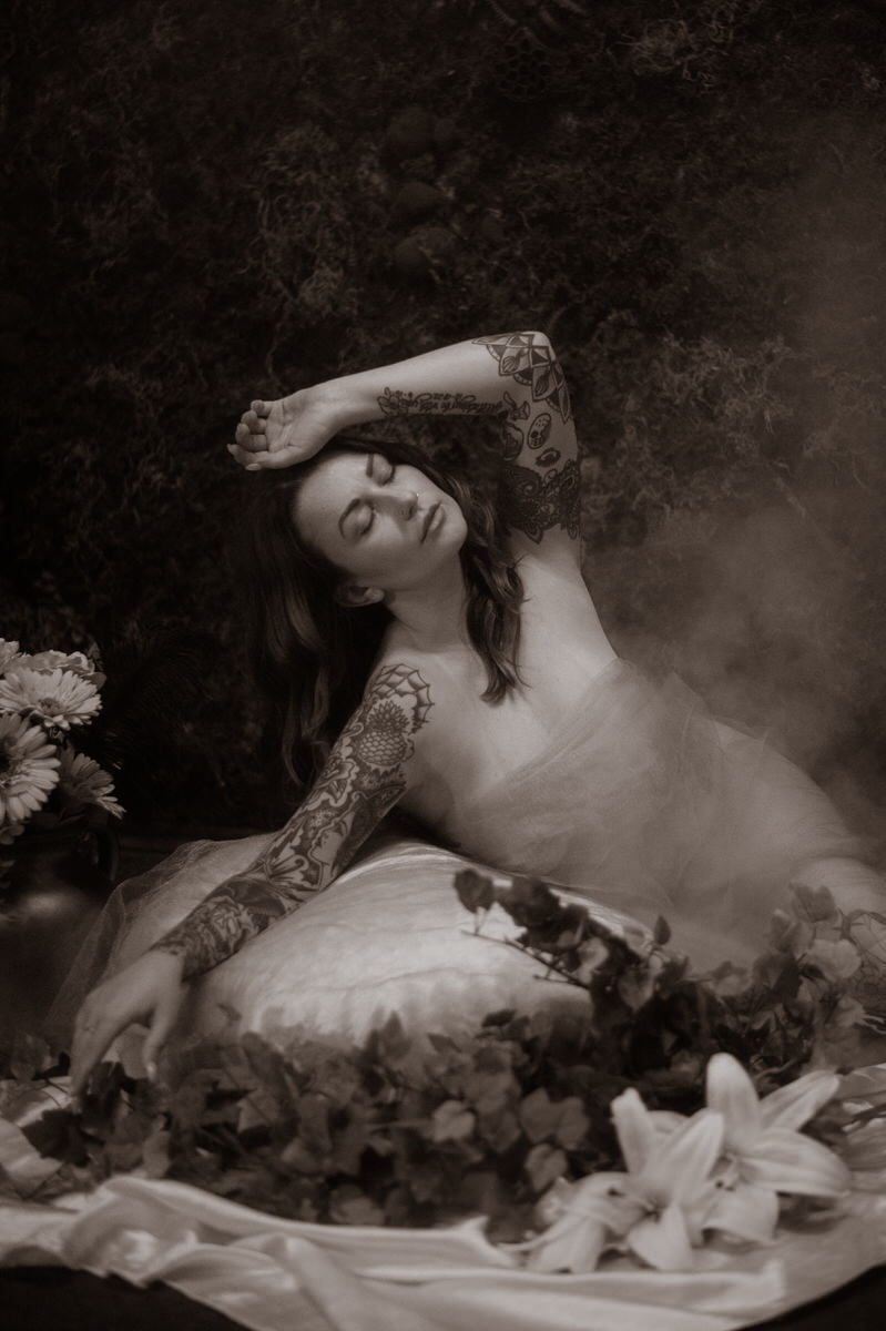 A black and white photo of a woman laying on a bed adorned with flowers, captured in a Dallas luxury boudoir studio.