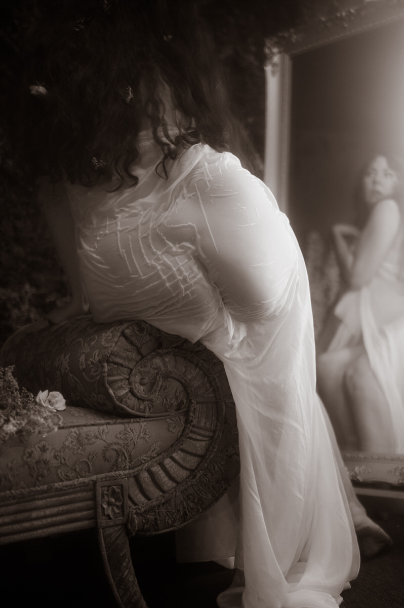 A woman in wet fabric posing in front of a mirror for a fine art boudoir photoshoot.