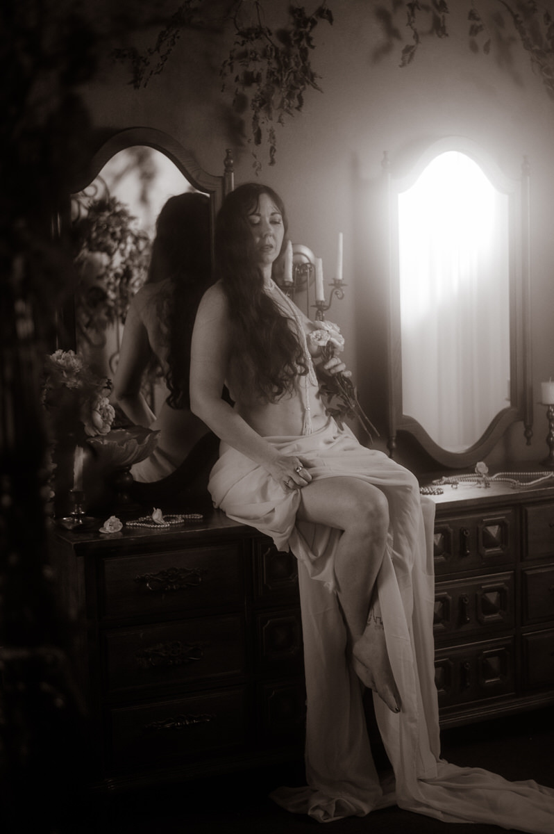 A woman sitting on a dresser, captured in a boudoir photography studio in Dallas by a fine art Texas boudoir photographer.