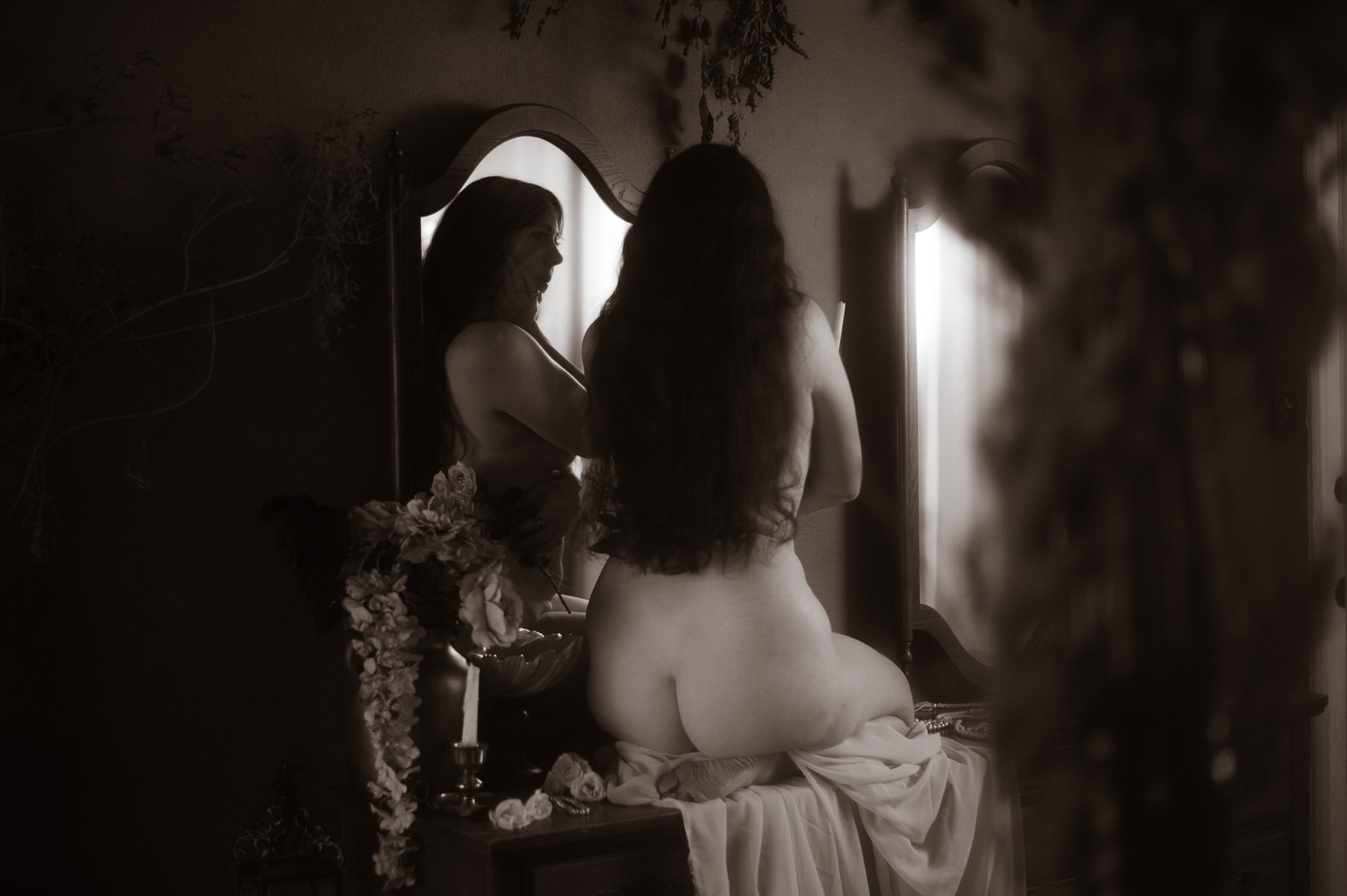 A fine art nude woman is sitting in front of a mirror.