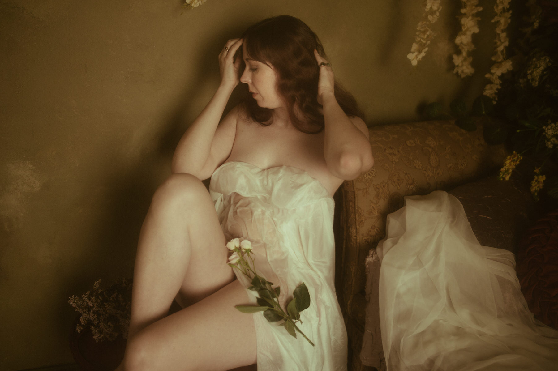 A woman posing in wet fabric adorned with flowers sitting on a bed, captured by a Texas boudoir photographer.