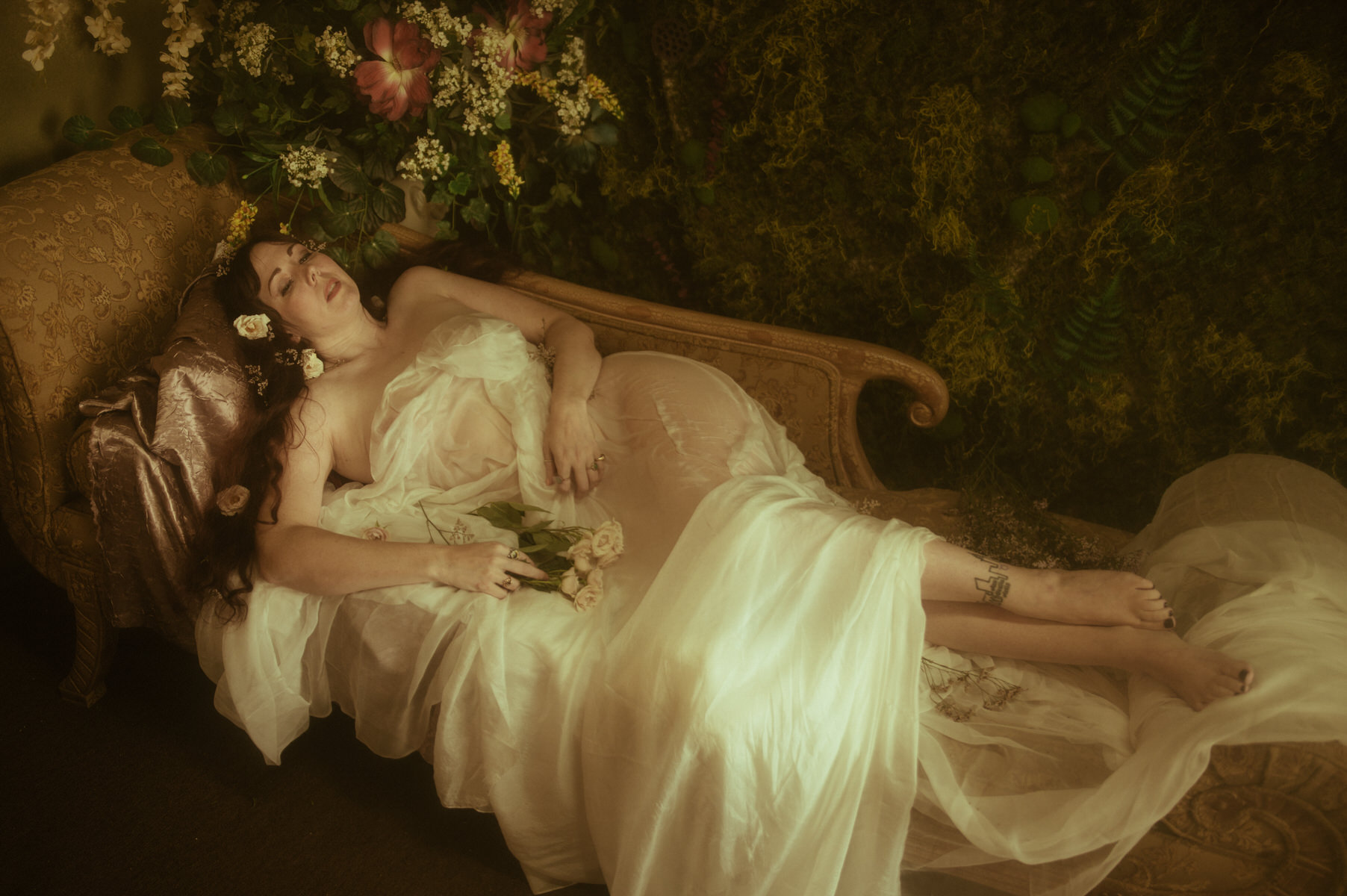 A woman covered in wet white silk, embodying renaissance inspired Texas boudoir session, effortlessly lounges on a bed.