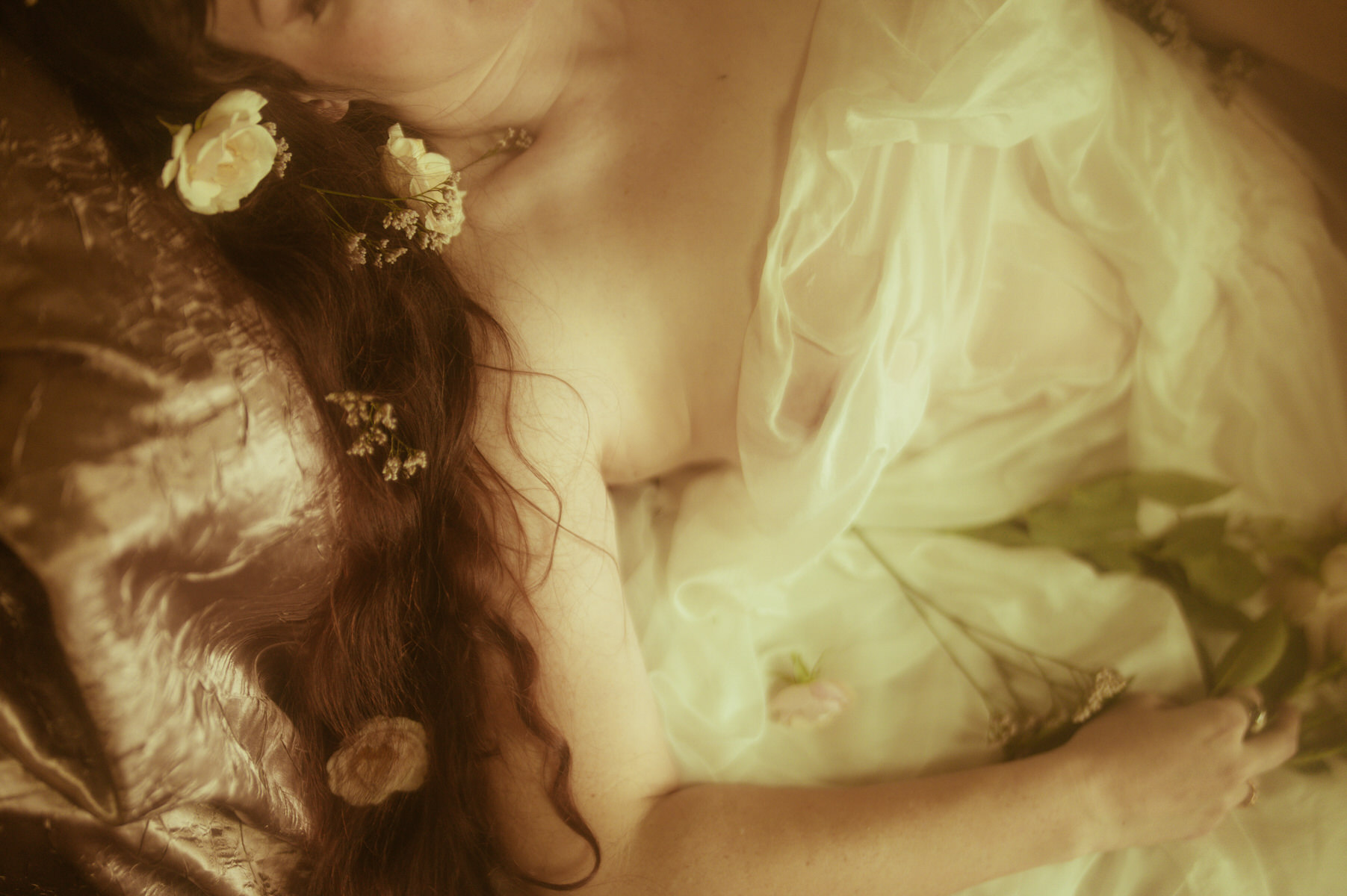 A woman in a boudoir photography setting, laying on a bed with flowers in her hair.