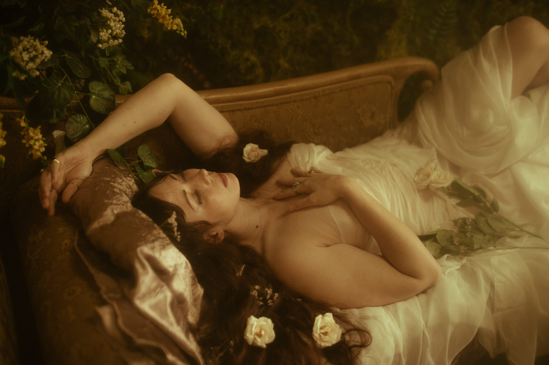 A woman draped in white silk fabric captured in a painterly photo while laying on a bed.