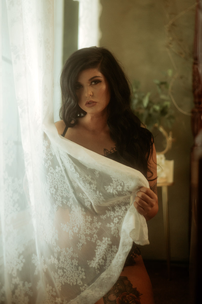 A woman with tattoos posing in front of a window for a Texas boudoir photography session.