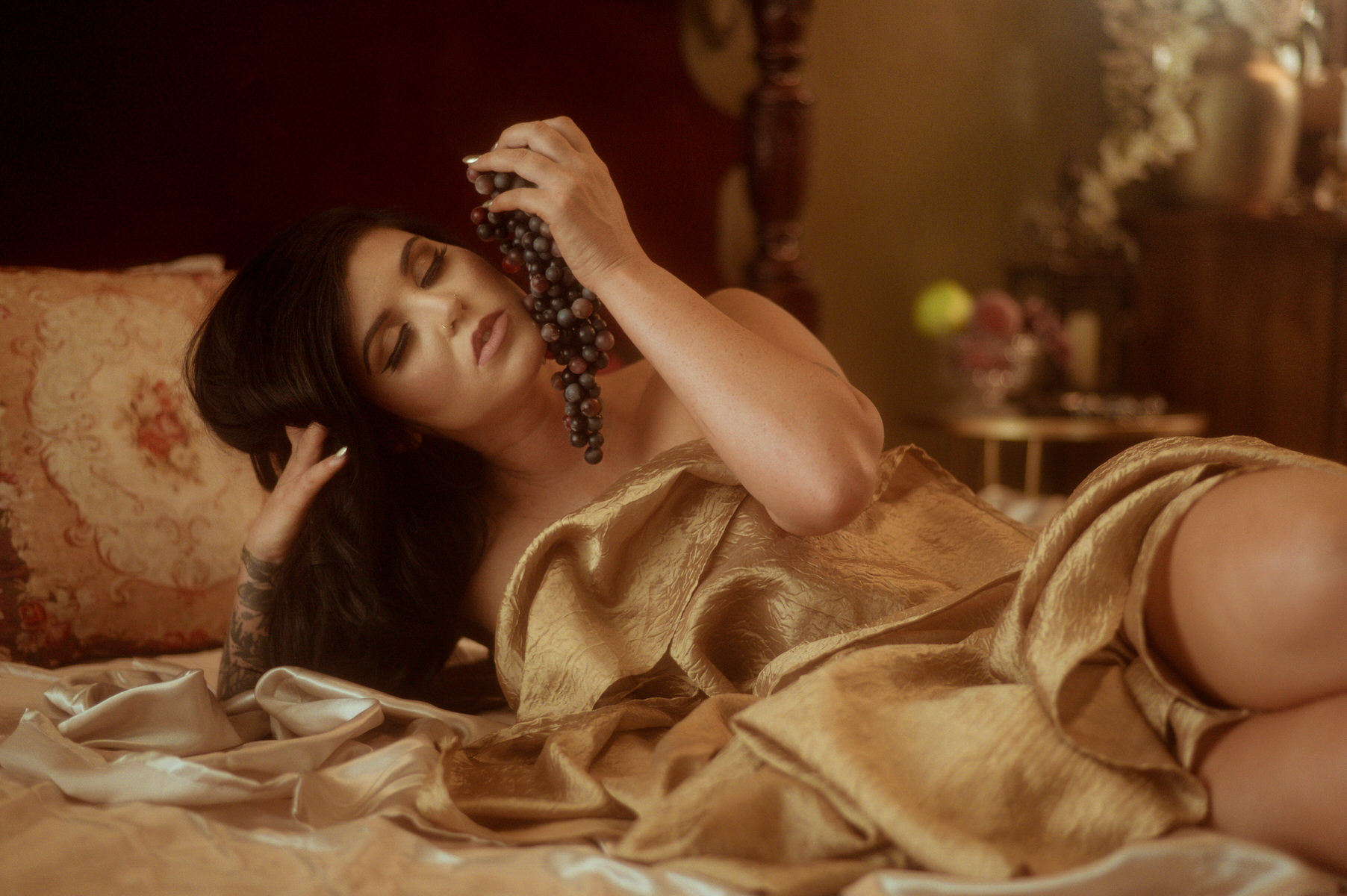 A woman in a gold dress, posing artfully on a bed in an exquisite display of fine art boudoir.