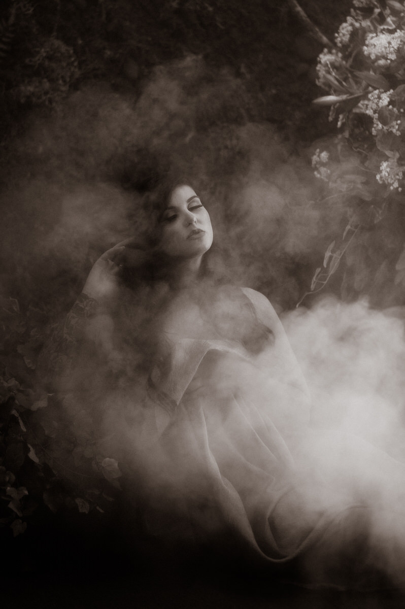 A black and white luxury boudoir photography of a woman laying in the fog.