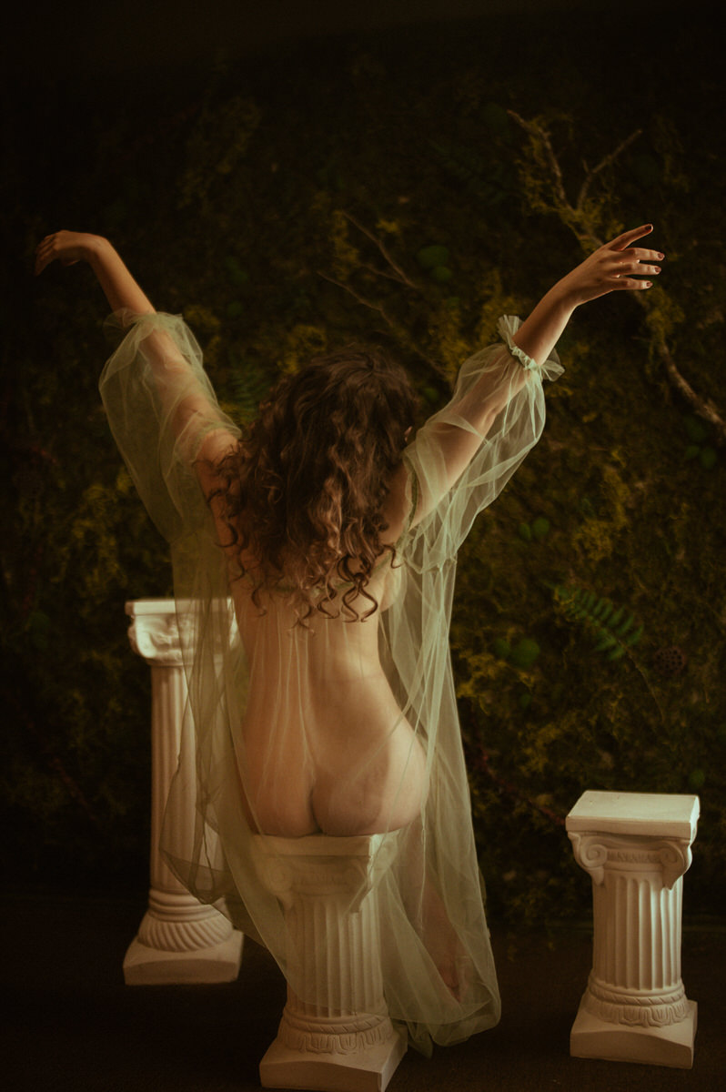 A painterly boudoir session featuring a woman posing on a set of pillars.