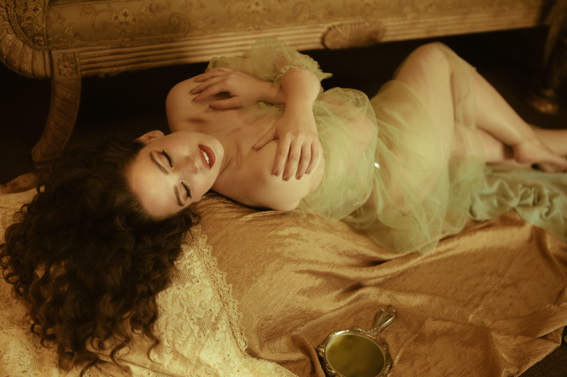 A fine art boudoir photograph of a woman in a green dress, gracefully laying on a bed.