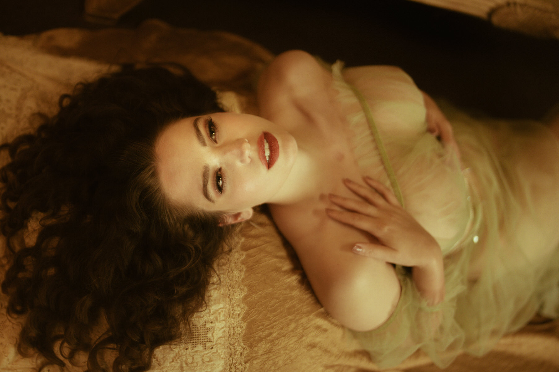 A pre-Raphaelite-inspired boudoir photo of a woman in a green dress laying on a bed.