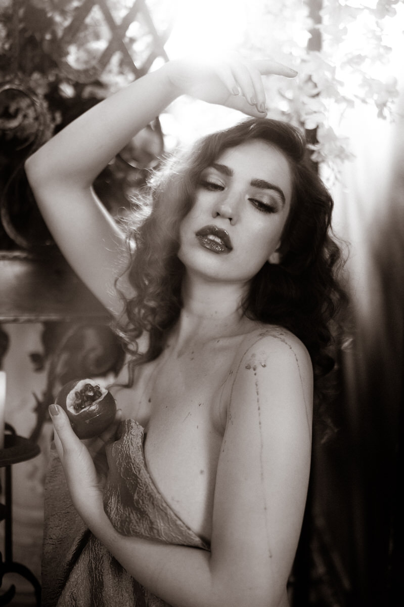 A black and white fine art boudoir photo of a woman holding a pomegranate.