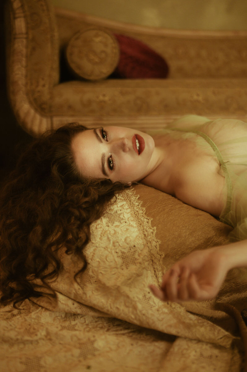 A Dallas boudoir fine art photo of a woman laying on a couch, inspired by pre-Raphaelite aesthetics.