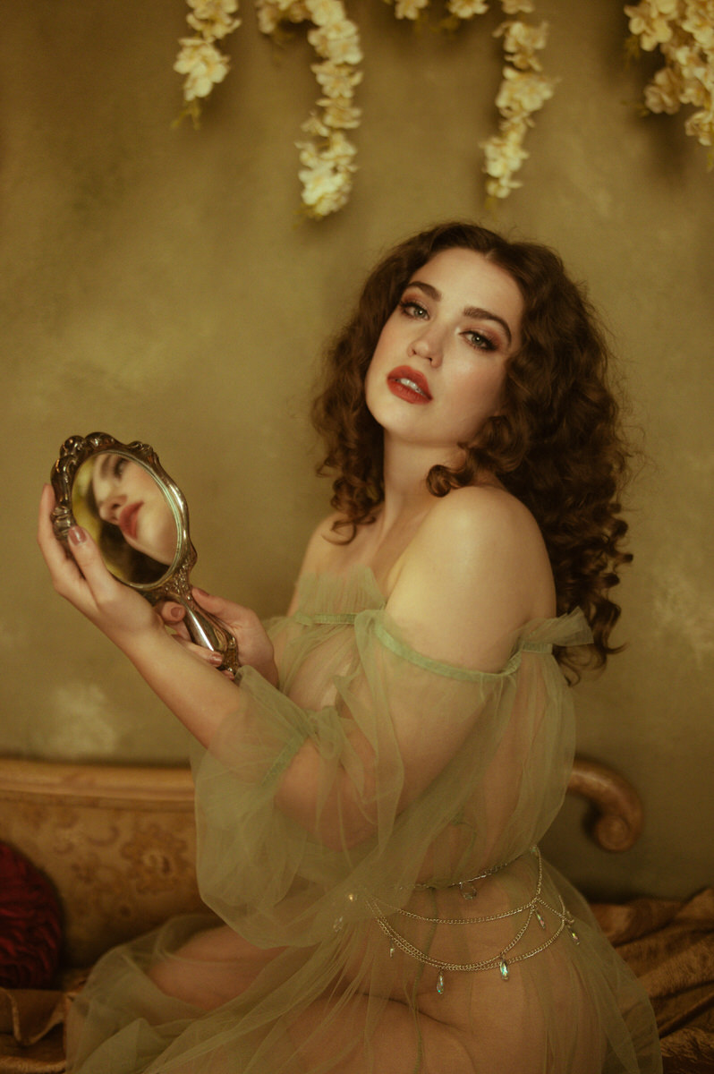 A woman in a green dress holding a mirror, capturing the essence of fine art boudoir photography.