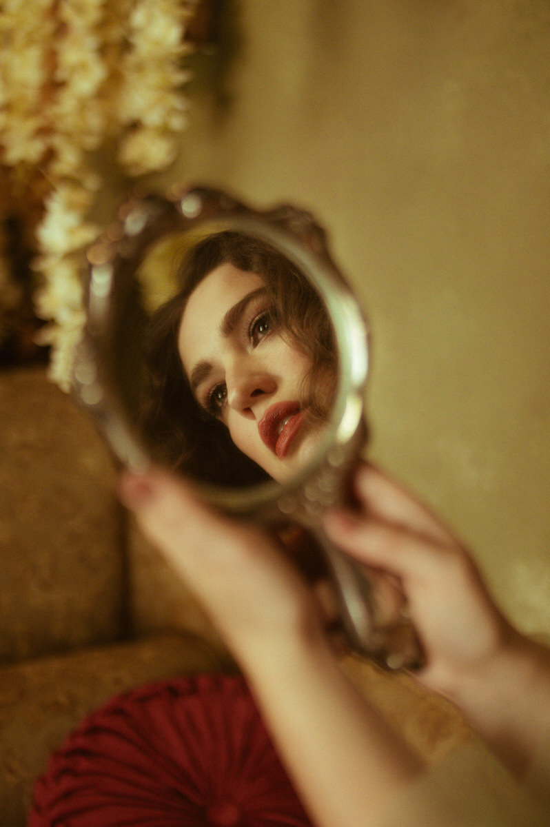 A woman is looking at herself in a hand mirror during a fine art boudoir photoshoot in Dallas.
