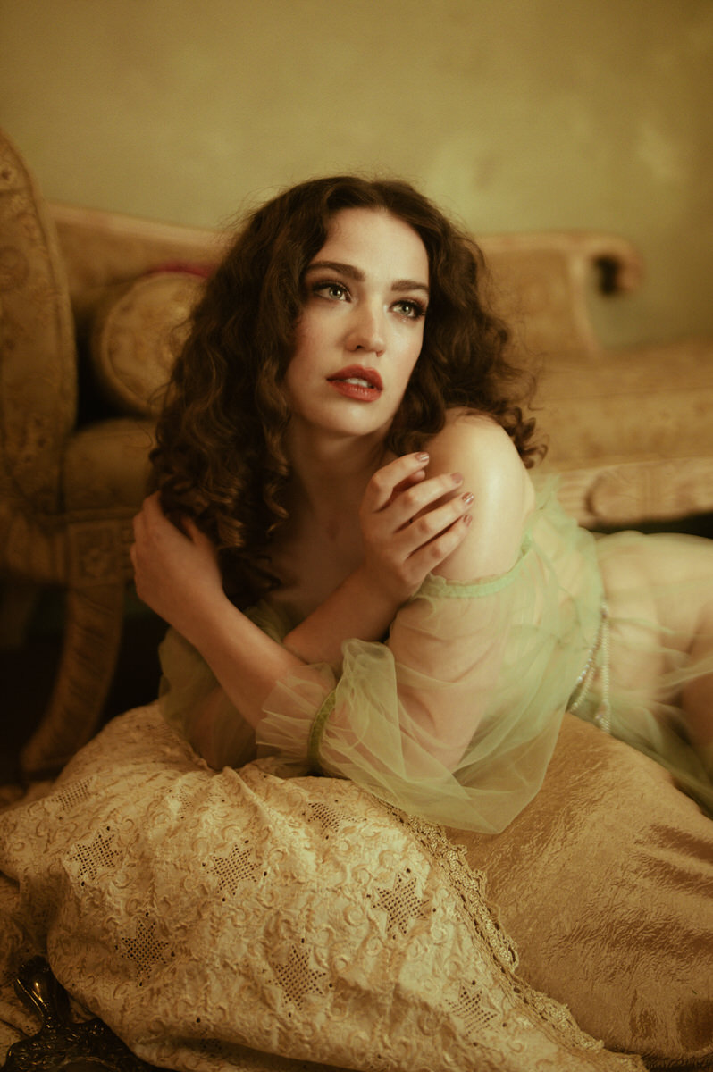A pre-Raphaelite-inspired woman in a green dress elegantly reclining on a fine art boudoir couch in Dallas.