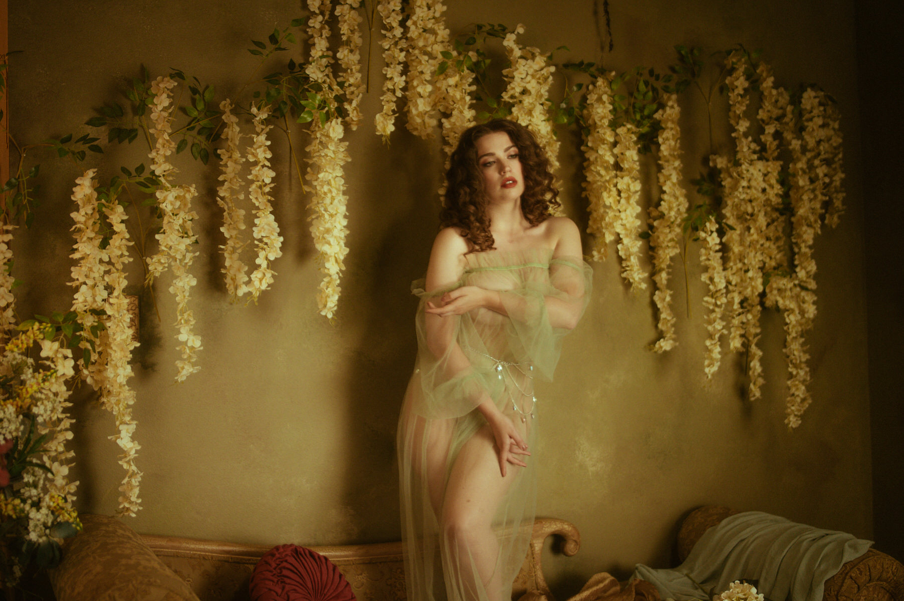 A woman in a sheer dress posing in front of flowers for a fine art boudoir photography session in Dallas.