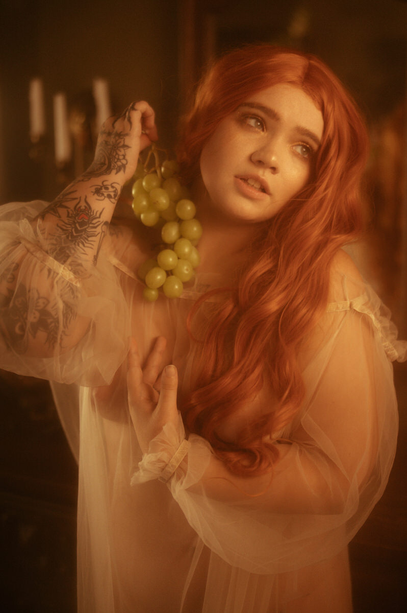 A woman with red hair sensually holding a bunch of grapes, perfect for boudoir portraits.
