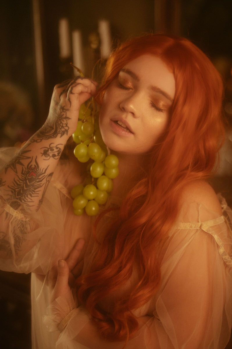 A beautiful woman with red hair posing with green grapes for a fruit inspired photoshoot in Dallas.