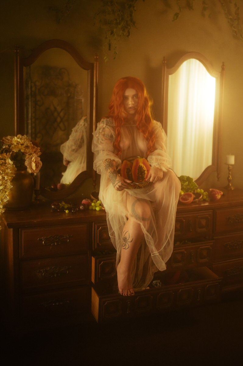 A woman with red hair sitting in a dresser surrounded by fruit for a boudoir photoshoot.