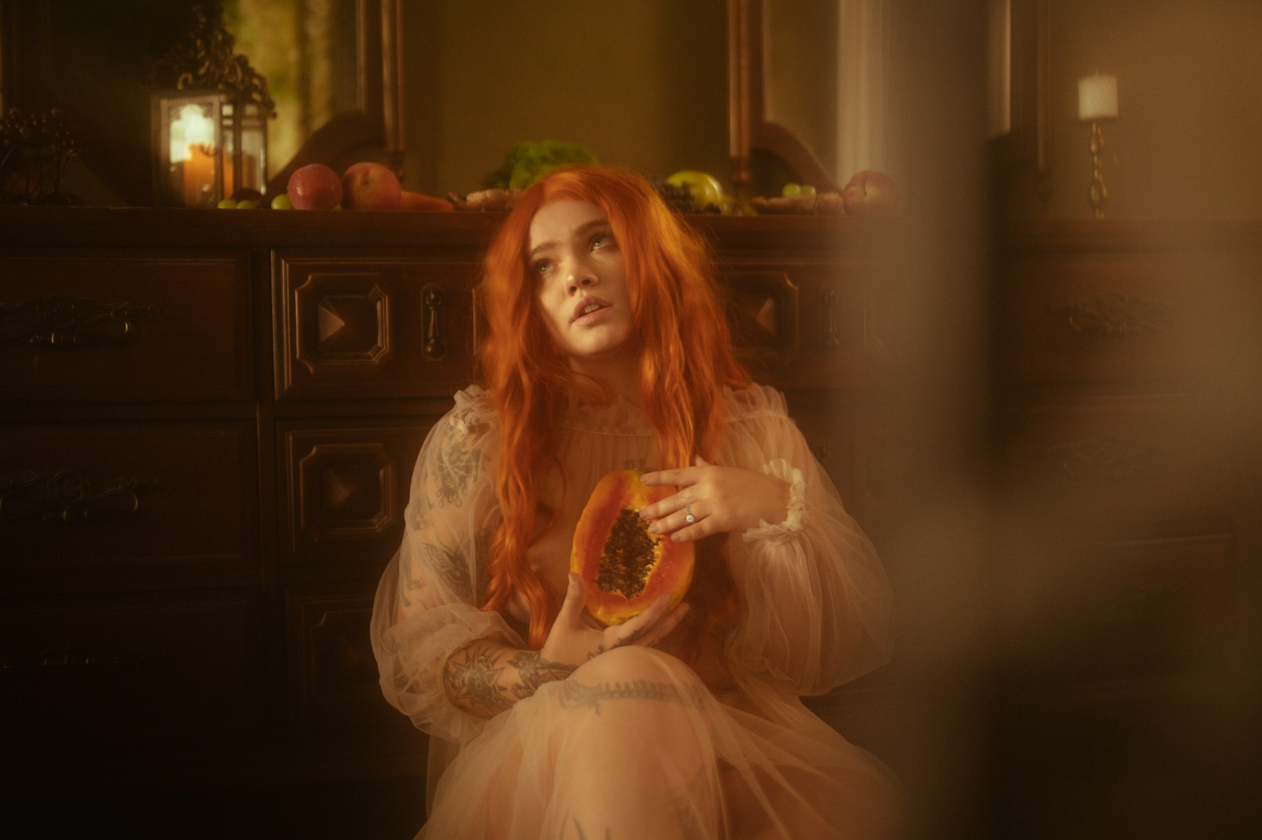 A woman with red hair sitting in a room surrounded by fruit during a boudoir portraits session.