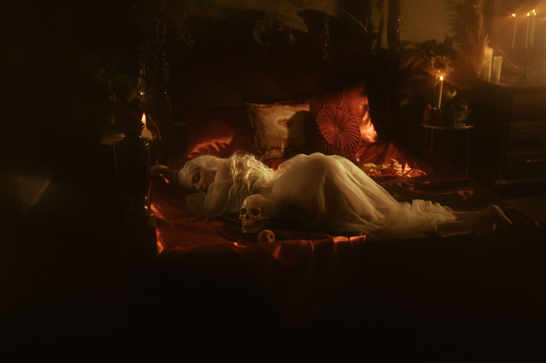 A woman in a white robe laying on her stomach on a bed with candles posing for a boudoir photoshoot.