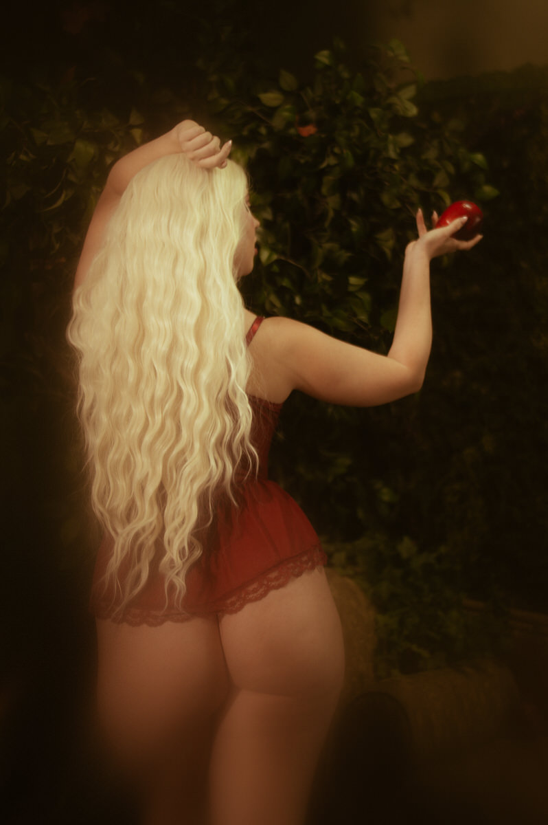 A woman with long blonde hair holding an apple in lingerie.