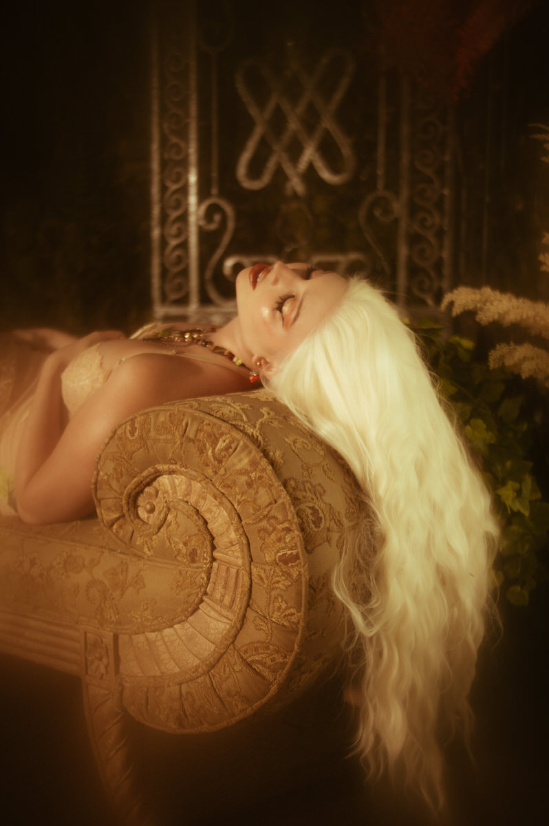 A woman with long white hair lounging on a couch, captured in boudoir photography style in Dallas.