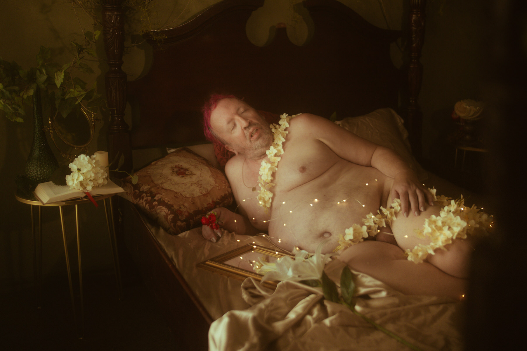 A naked man laying on a bed with flowers, capturing self love through photography.