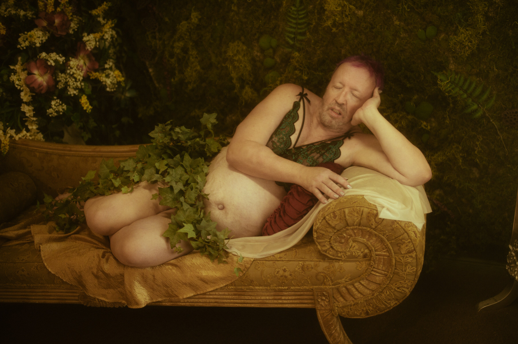 A trans woman laying on a couch covered in ivy.
