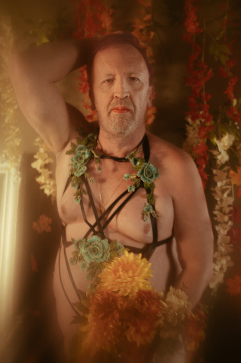 A trans woman posing in lingerie with flowers at a photoshoot.