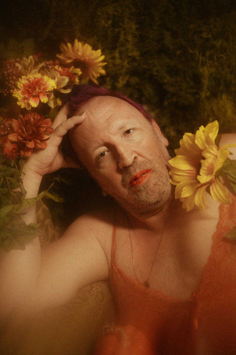 A trans woman laying on a bed with flowers in her hair during a self love photography session at a Dallas boudoir studio.
