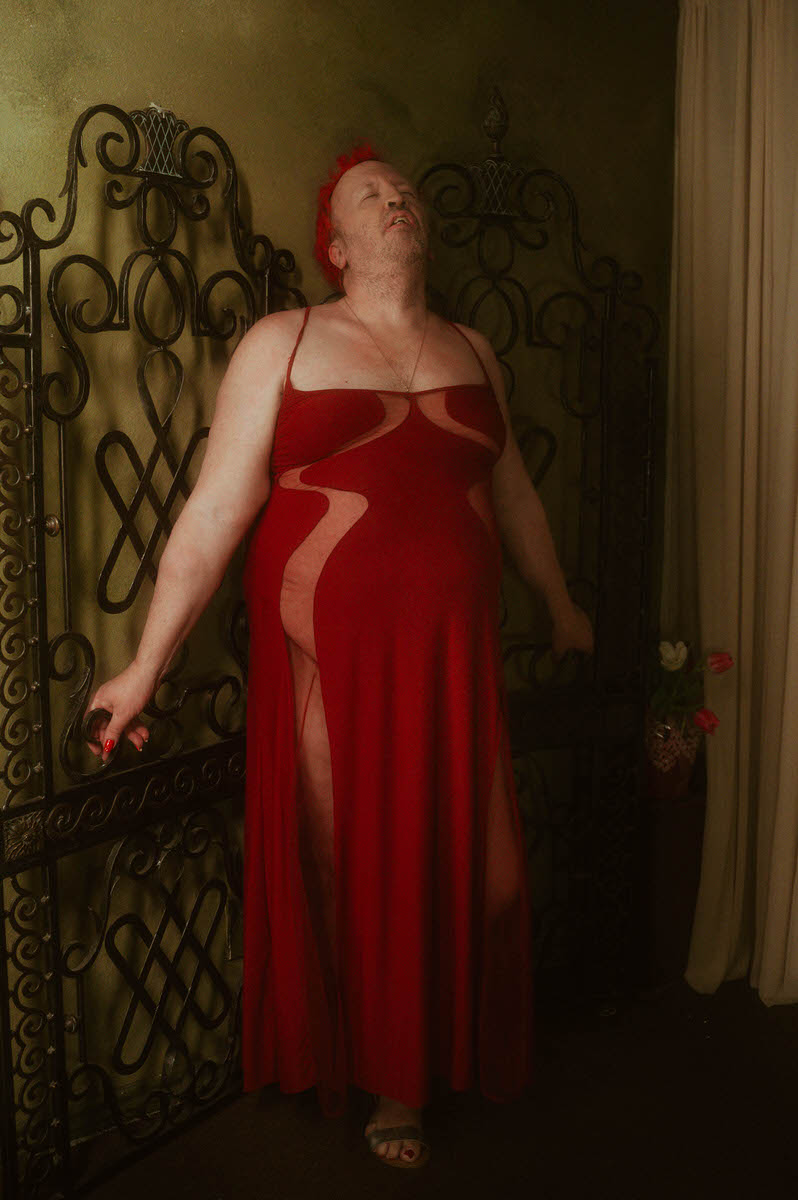 A trans woman wearing a red Thistle Inspired dress for a boudoir photoshoot.